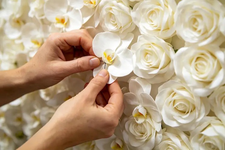 artisan handcrafting white flower wall backdrop with stand